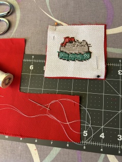 Starting to finish a Pusheen ornament Finished cross stitch piece pinned to red fabric